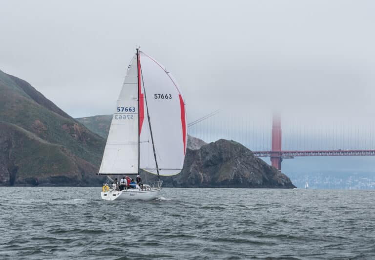 The Santa Cruz 33, Siren, sails towards the Golden Gate bridge with a spinnaker up. It is a cloudy and misty day.