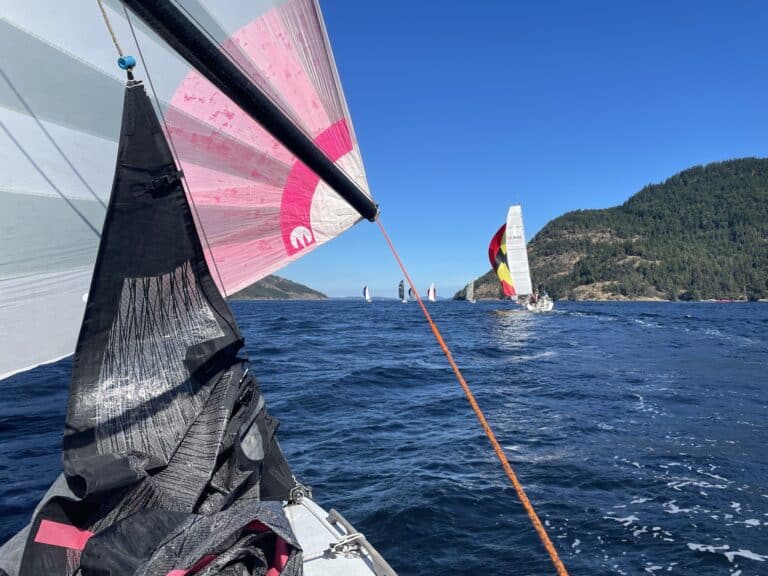 UK Sailmakers Moore 24 Amoore with a pink spinnaker races to catch boats ahead. Blue sky day on the ocean with some green treed islands in the distance.