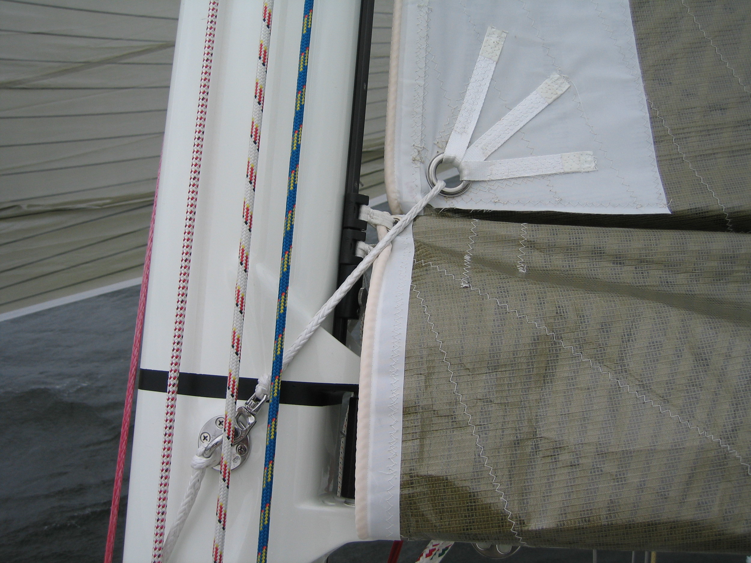 Photo 3:&nbsp;The reef tack his held by the white Dyneema line that comes from a padeye on the far side of the mast, through the reef tack grommet where it snaps into place on the padeye located below the black measurement band.